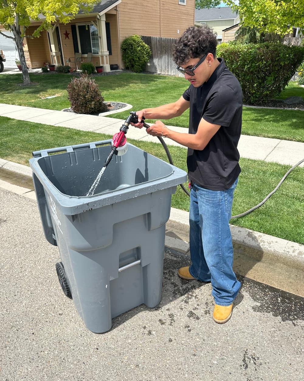 Zeke rinsing the inside of a trash bin at the curb